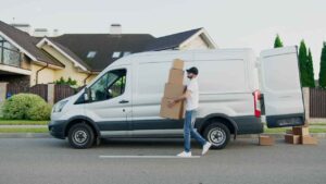 Man carrying multiple cartons from car during trading hours for Coles supermarket
