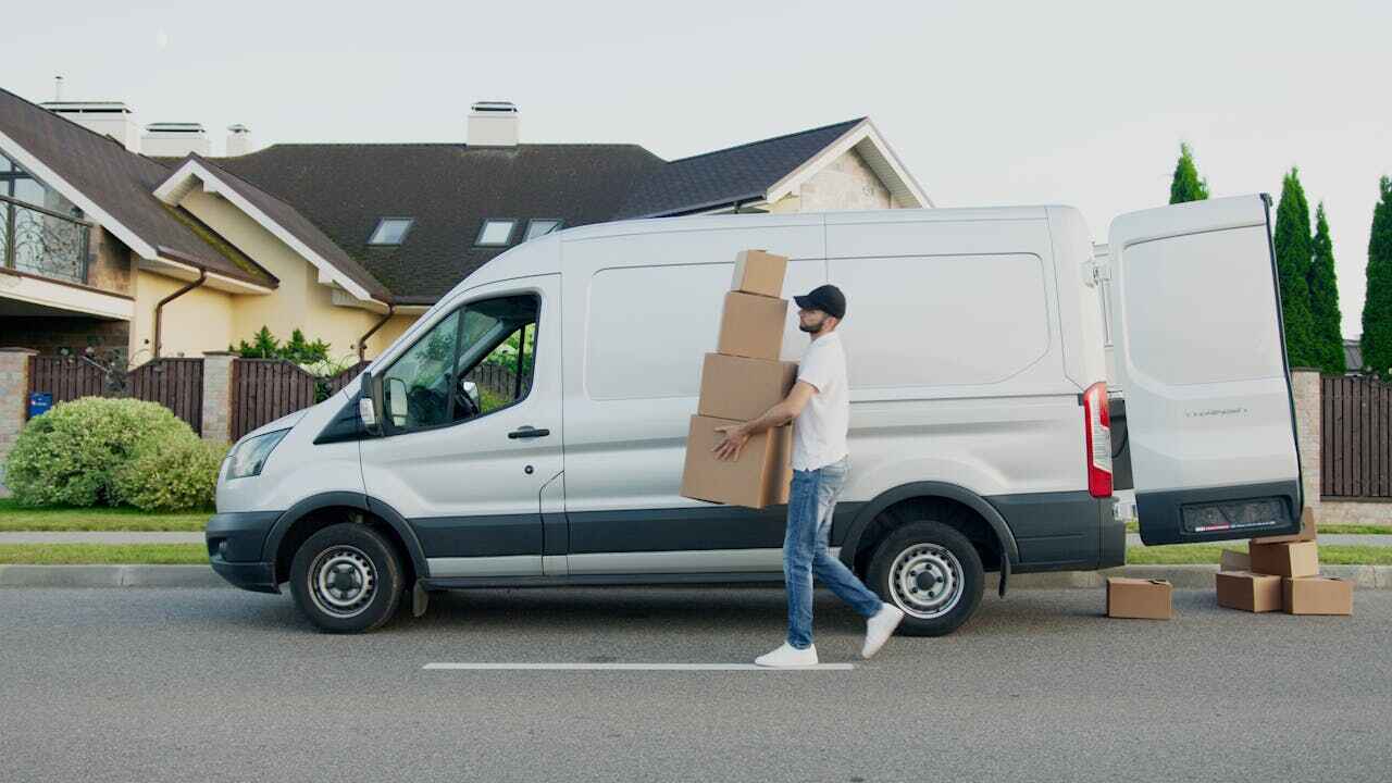 Man carrying multiple cartons from car during trading hours for Coles supermarket